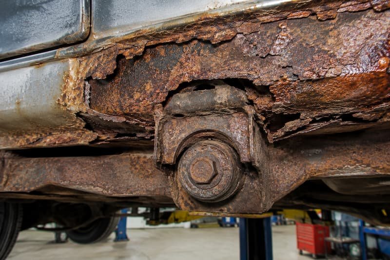 Scaled and flaking underbody panel around a body mounting point on a VW T25 on a workshop lift.