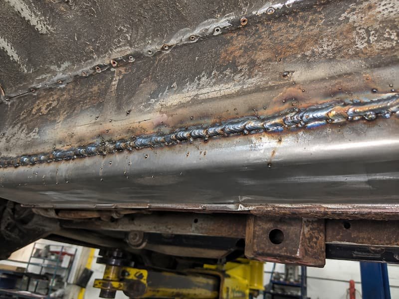 MIG welding on a vehicle sill panel in a workshop, showing the continuous seam weld on new steel fabricated to replace corroded metal.