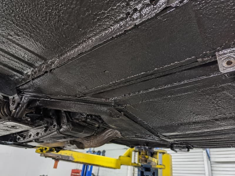 Van underside covered in black underseal concealing the condition of the steel underneath, showing how fresh coating hides active corrosion from view.