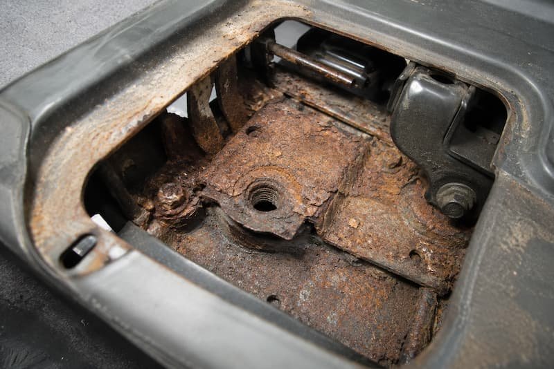 Scaly orange corrosion on internal bracketry and a mounting point inside the seat base aperture of a VW T25.