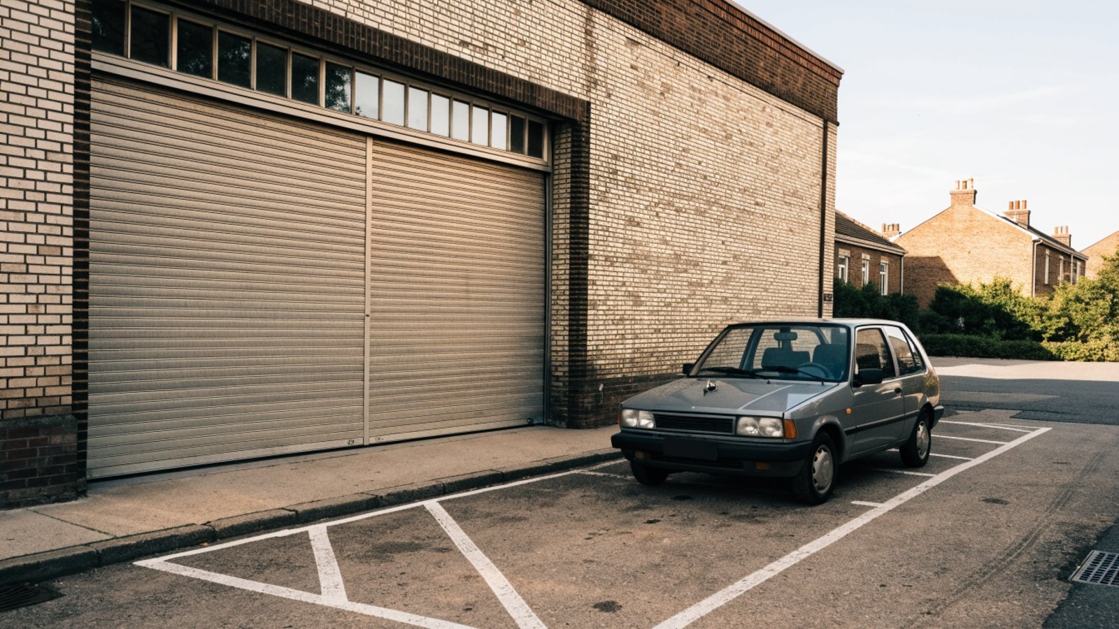 Small grey hatchback parked in a marked bay beside a garage building ready to be used as a courtesy car
