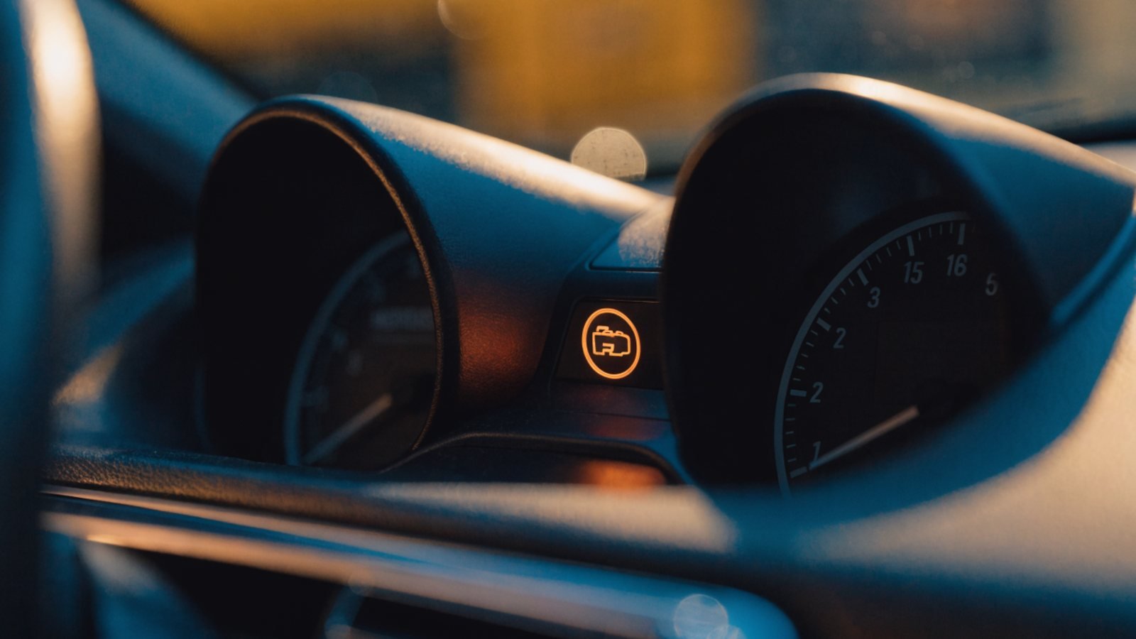 Car instrument cluster at night with an amber engine warning symbol lit between the dials