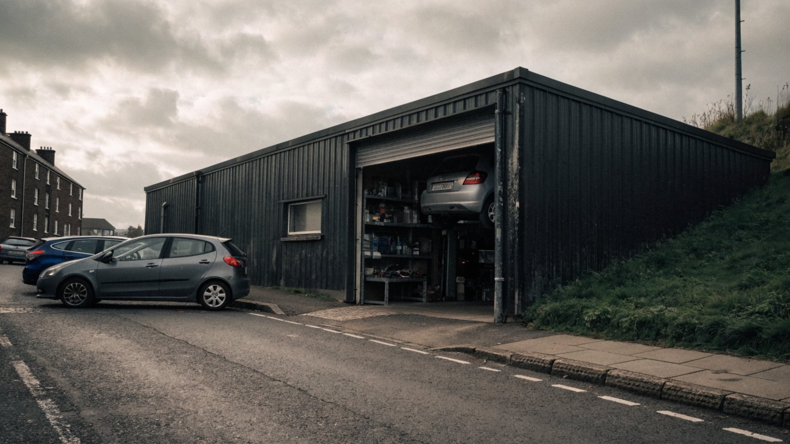 Independent garage in a low industrial unit on a quiet road with its roller door open and a car raised on a lift inside