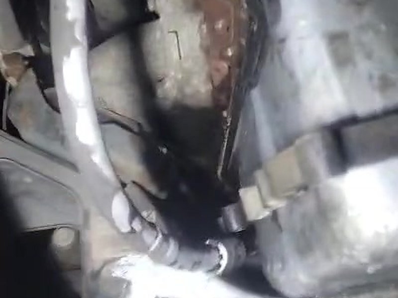 Underside of an Iveco van on a lift showing the oil-wet steel engine sump sitting directly above a corroded front subframe, with a pipe running alongside.