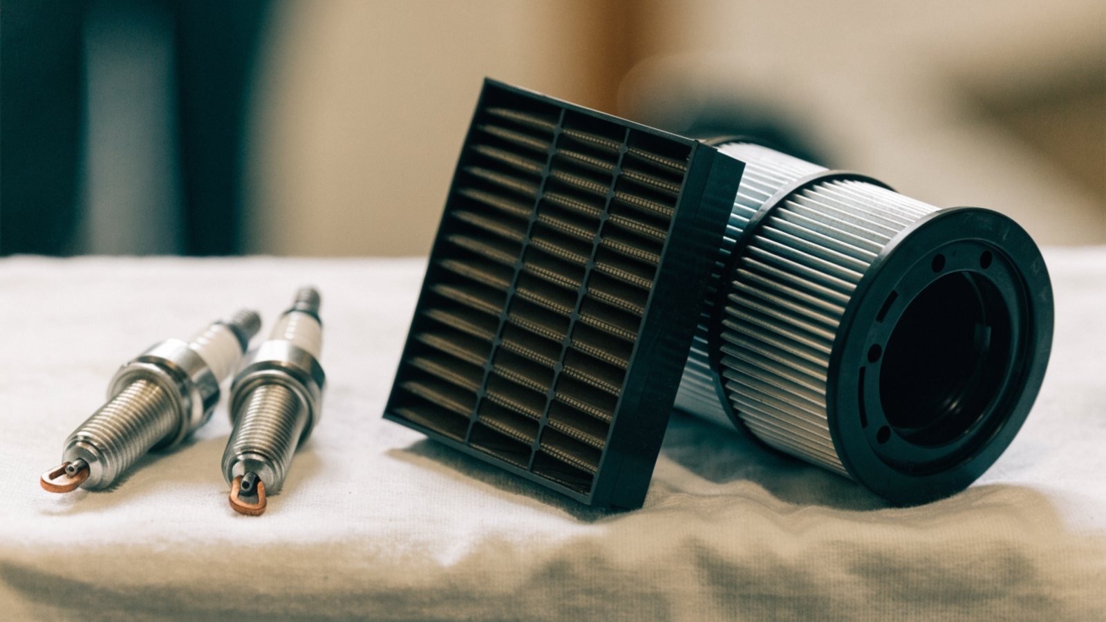 New spark plugs, a pollen cabin filter and an oil filter laid out on a clean workshop cloth