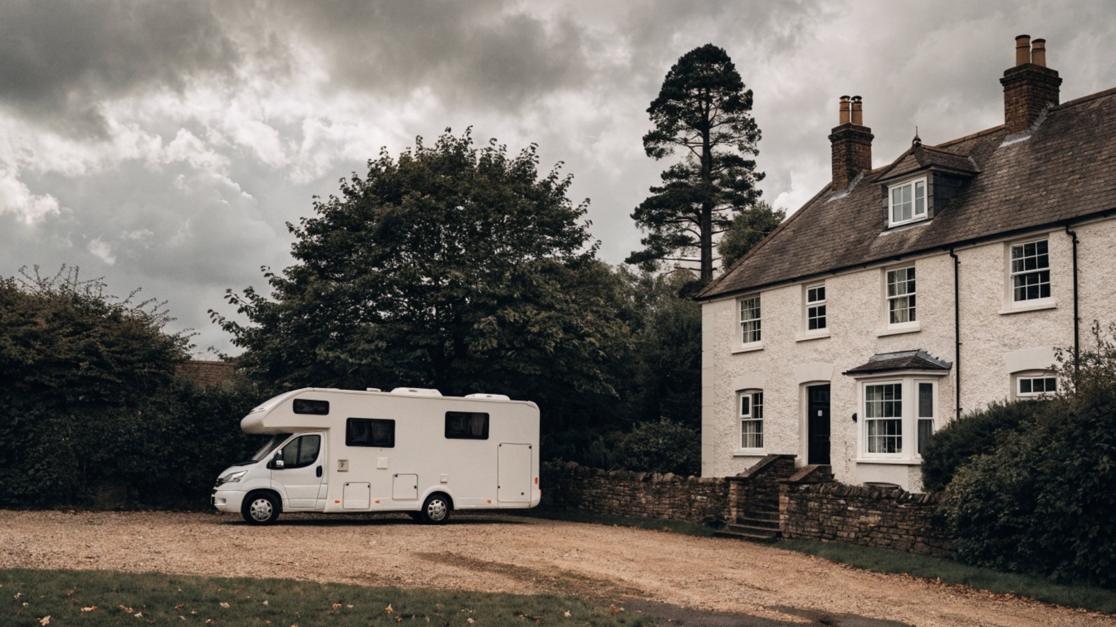 White motorhome parked on a gravel driveway beside a detached house on an overcast day