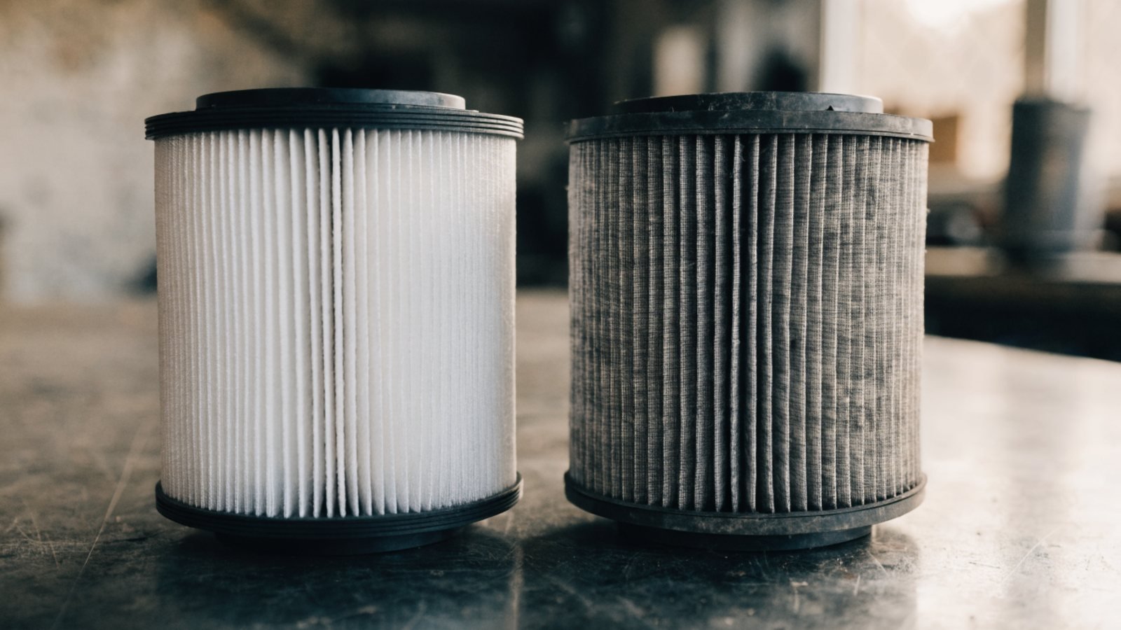 New white engine air filter next to a dirty grey used air filter on a workshop bench