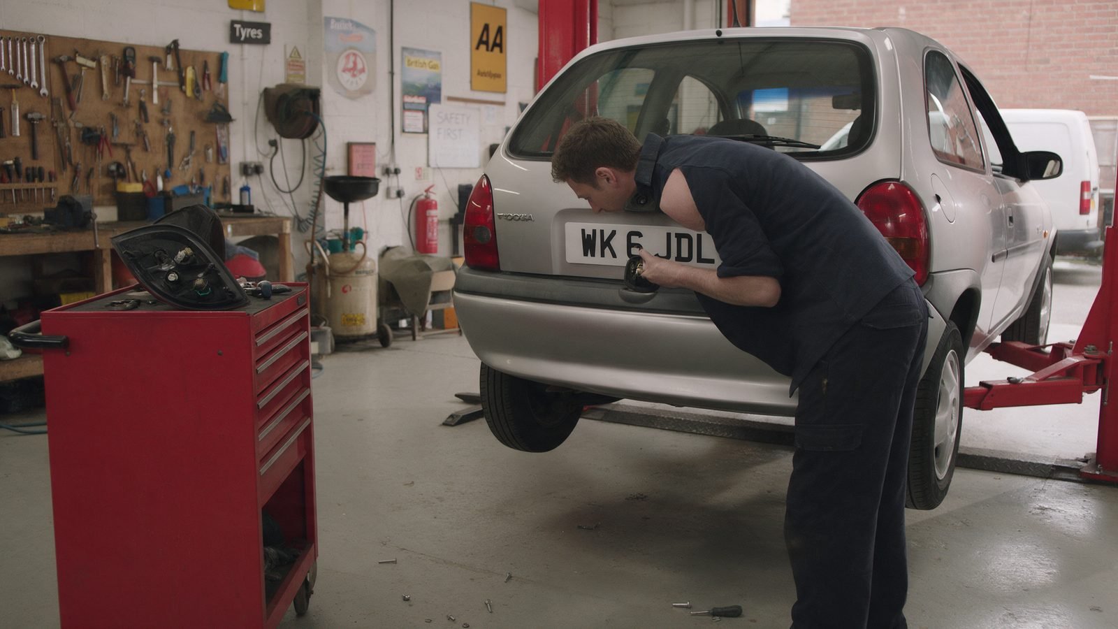 Mechanic replacing a rear number plate bulb on a hatchback with the light cluster removed